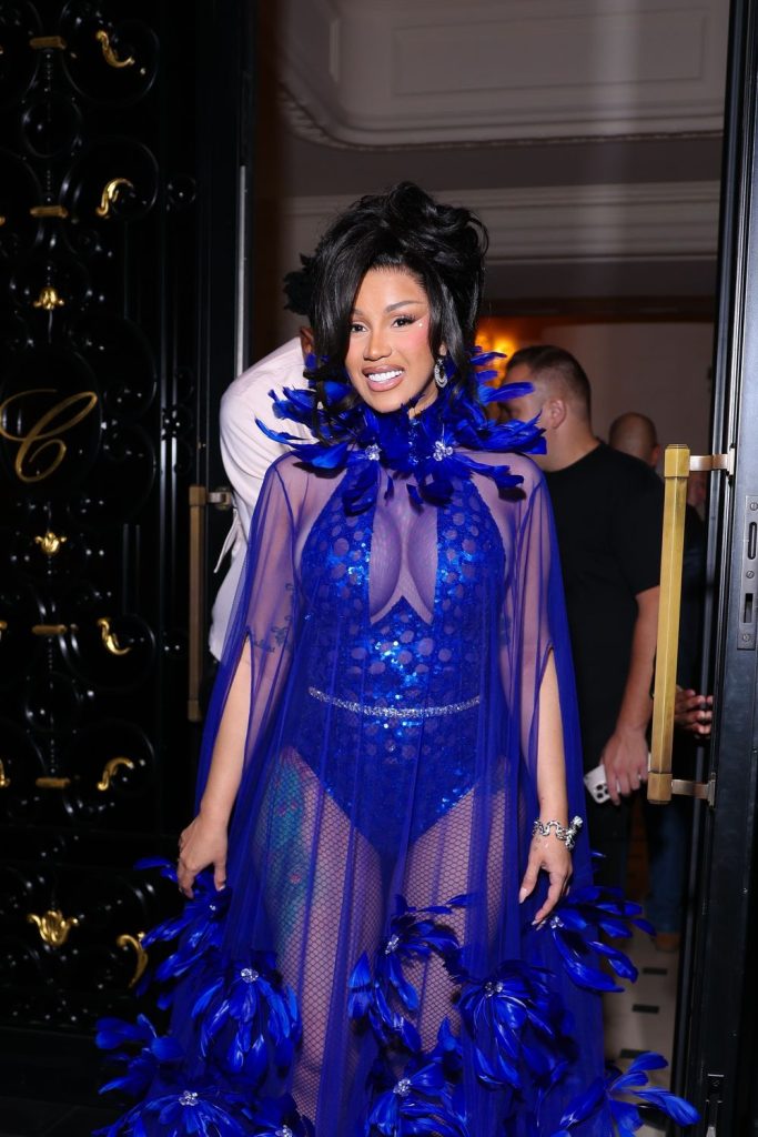 Cardi B wearing a sheer, sequined royal blue gown adorned with blue feathers.