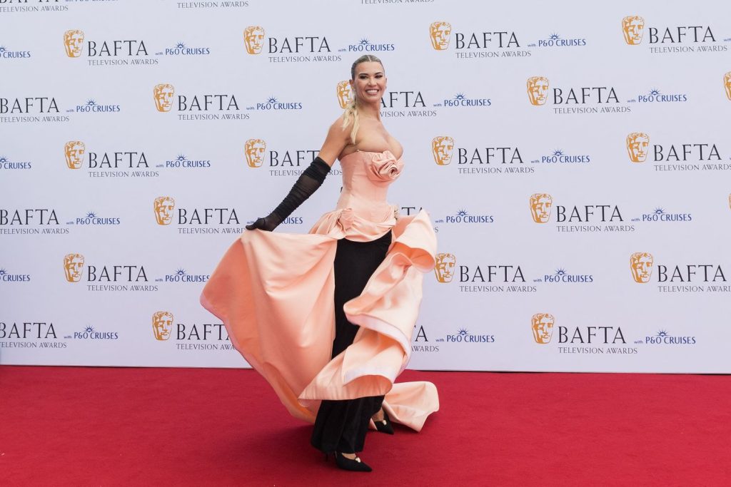 Christine Quinn poses on the BAFTA Television Awards red carpet in a peach and black gown with black gloves.