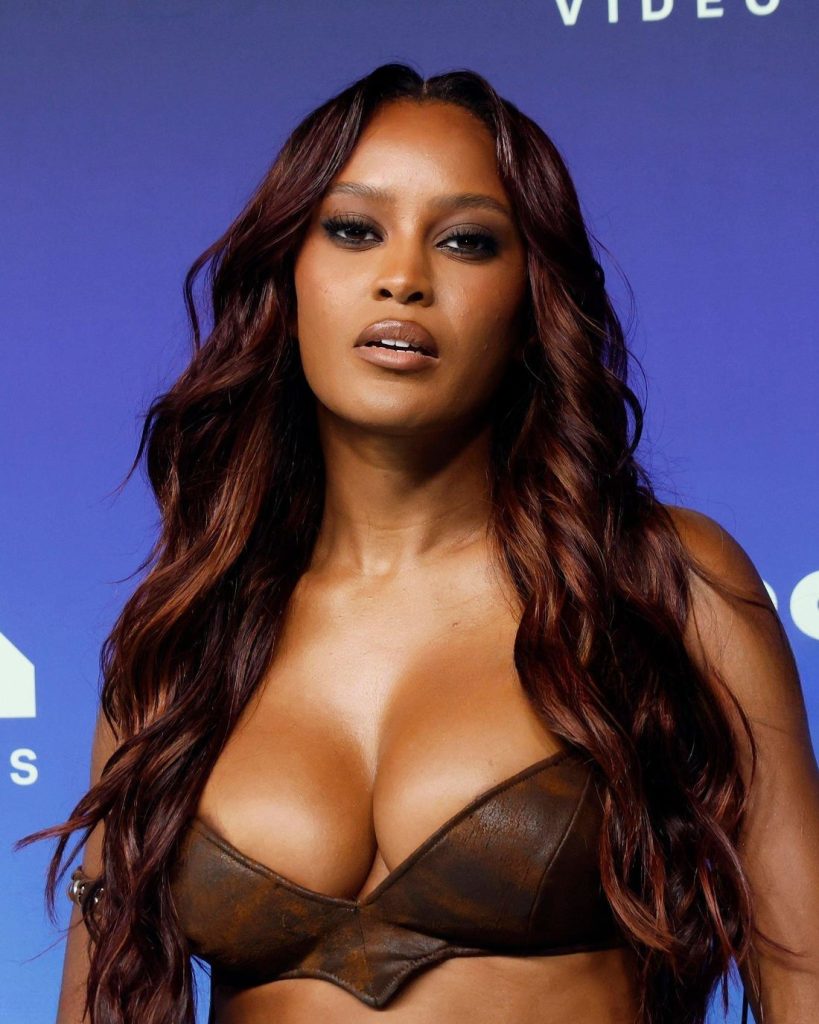 A woman with long wavy reddish-brown hair posing in front of a blue backdrop.