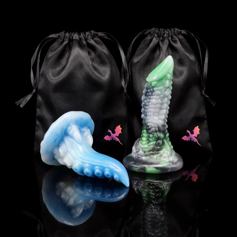 Two Dragon Dildo® Wyrm’s Own silicone sculpts on a black background, one blue tentacle design and one green and silver scaled design, each with a black satin bag