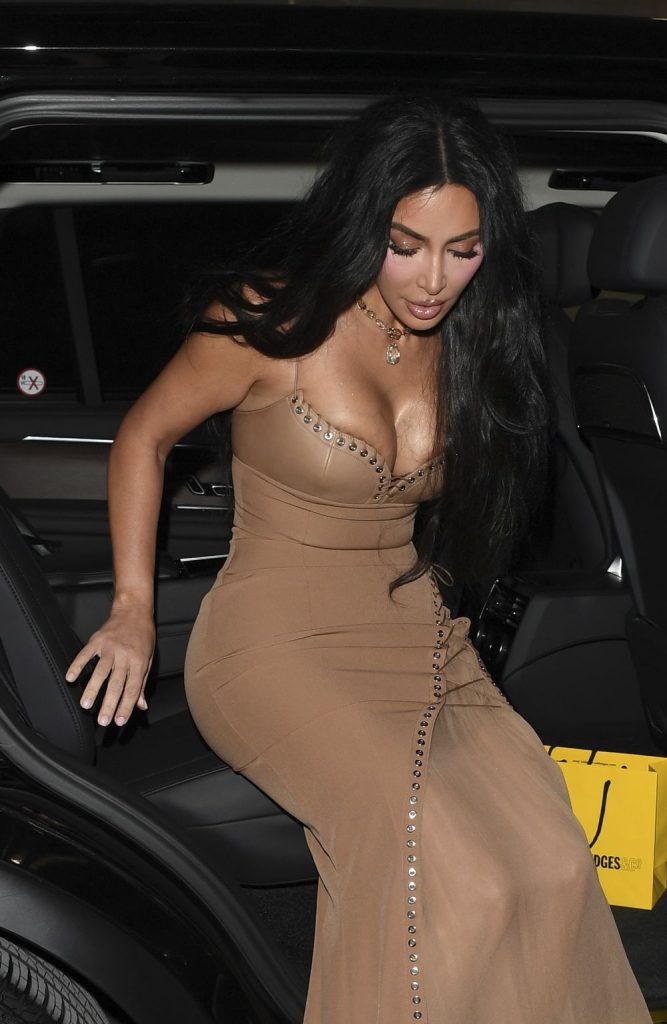 Kim Kardashian exiting a car wearing a tan, form-fitting dress with silver grommet details.